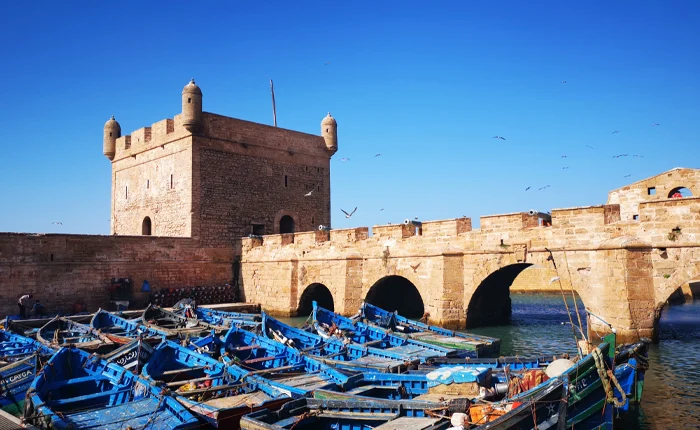 Private Essaouira Day Trip from Marrakech:The Skala du Port tower and the blue fishing boats of Essaouira harbour under a clear sky
