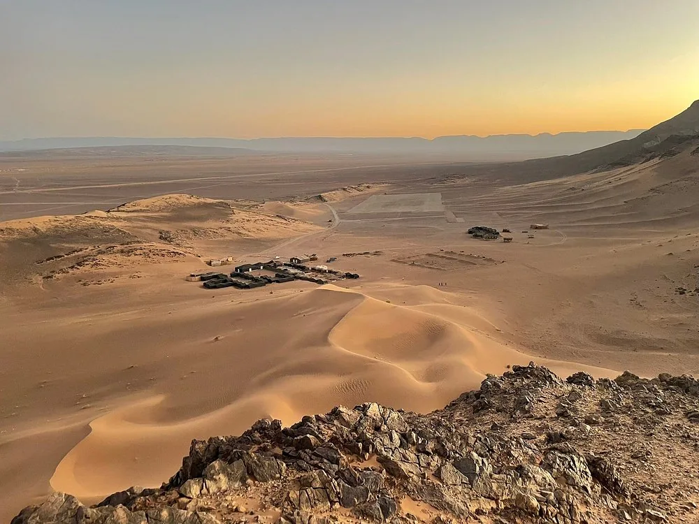 Petite dune de sable dans le désert de pierres près de Zagora, avec un camp et une plaine au loin